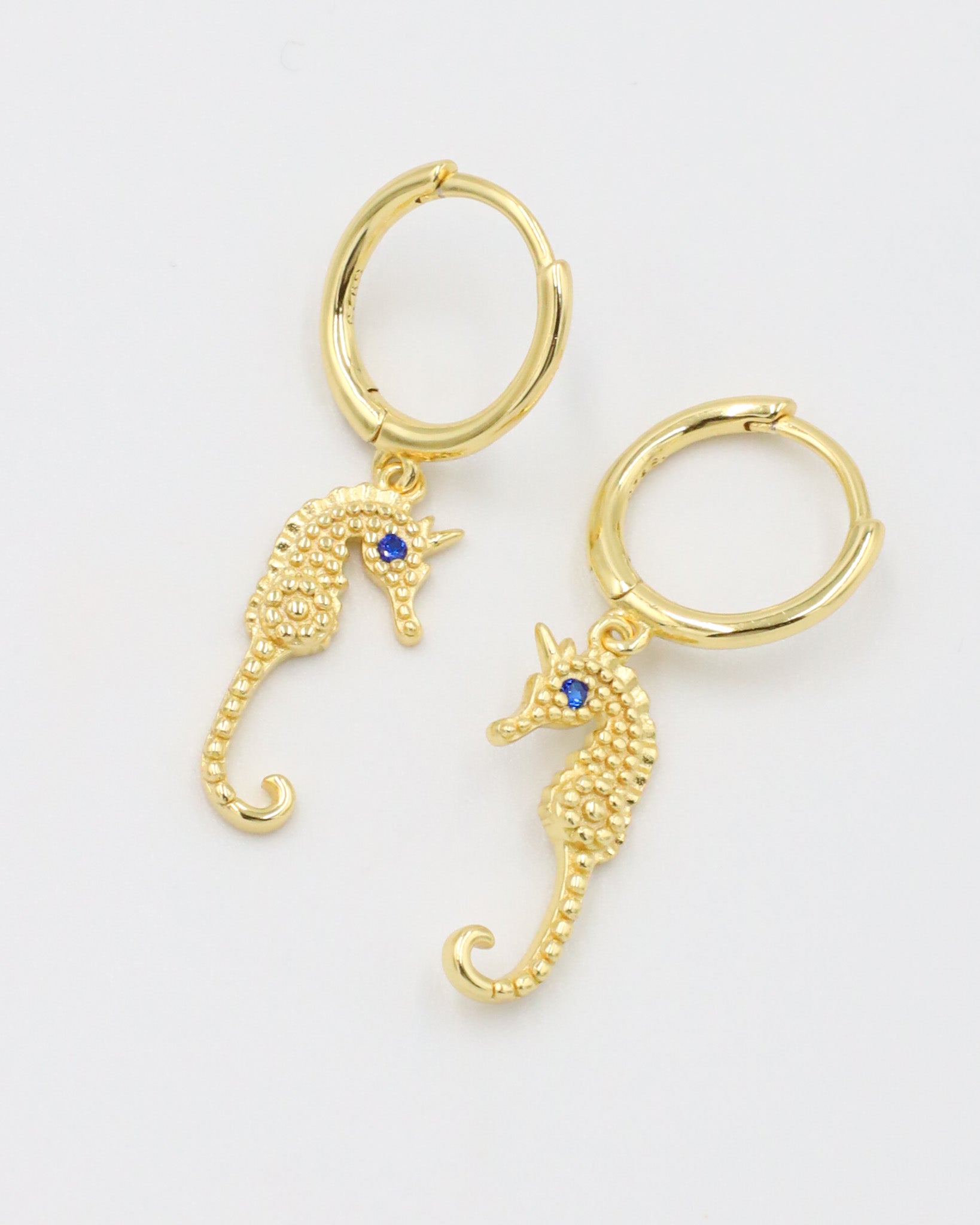 Pair of Seahorse Gold earrings made from gold-plated sterling silver, featuring seahorse charms with blue zirconia eyes.
