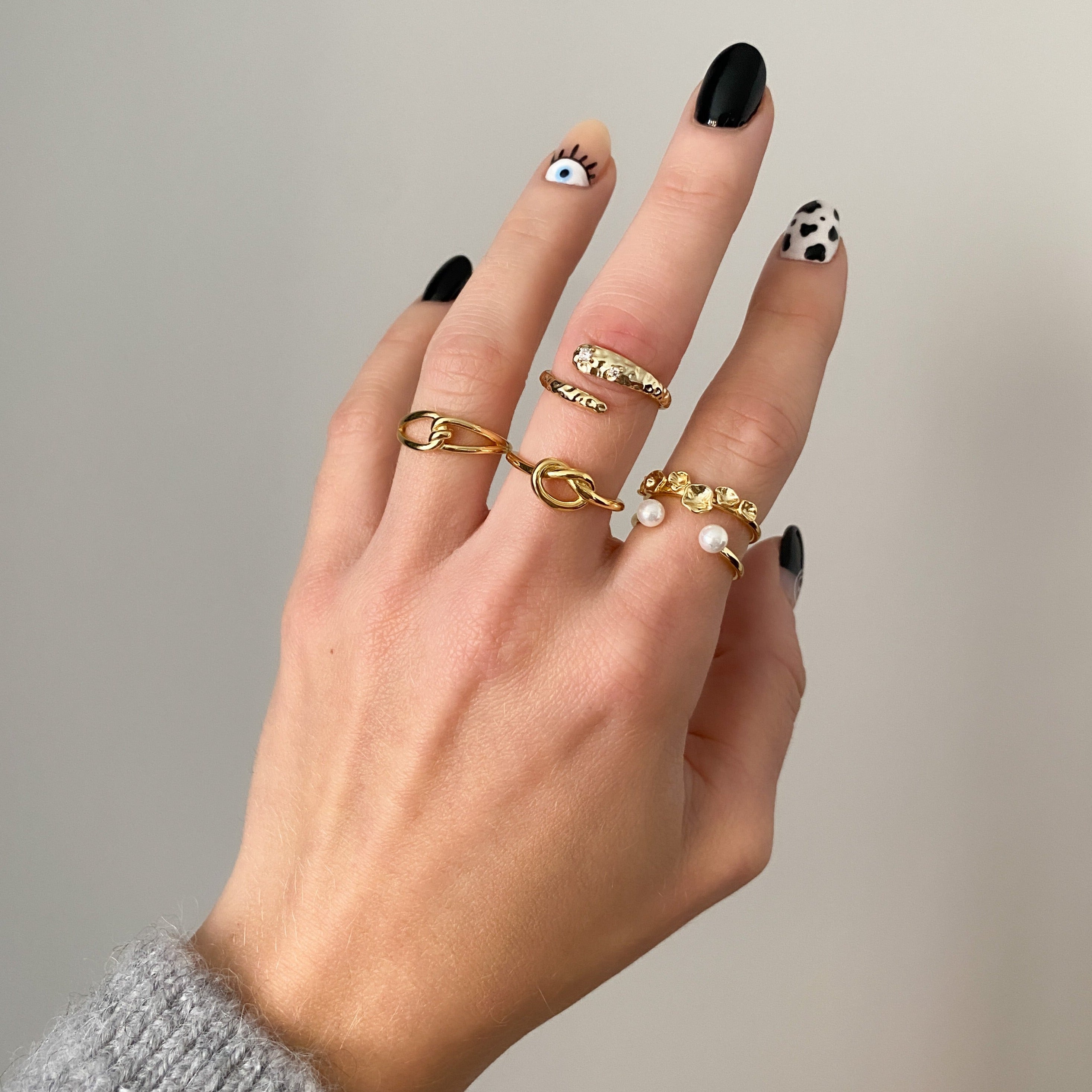 Hand with creative nail art showcasing a stylish mix of gold-plated 925 sterling silver rings, including hammered textures, pearl details, and minimalist statement designs – modern Swiss jewelry aesthetic.
