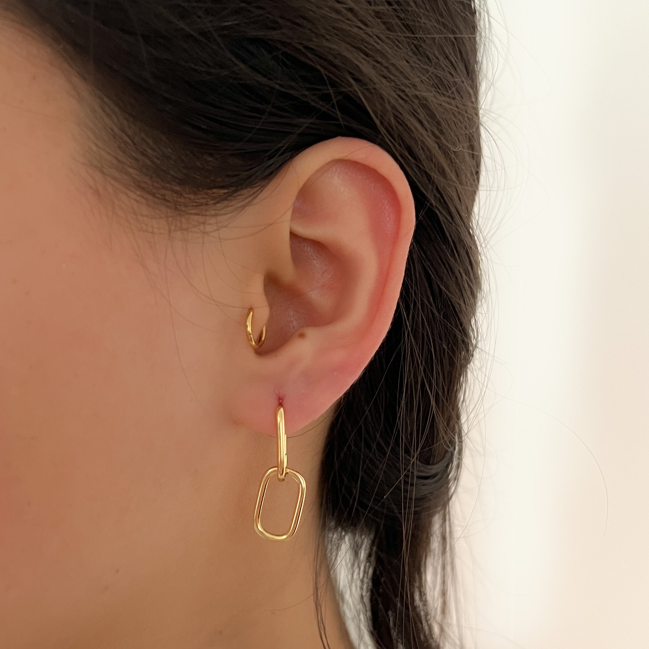 Close-up of a person wearing the Adelaide earring in gold on the lobe, paired with the Lu earring in the tragus, both from ruru. studios.