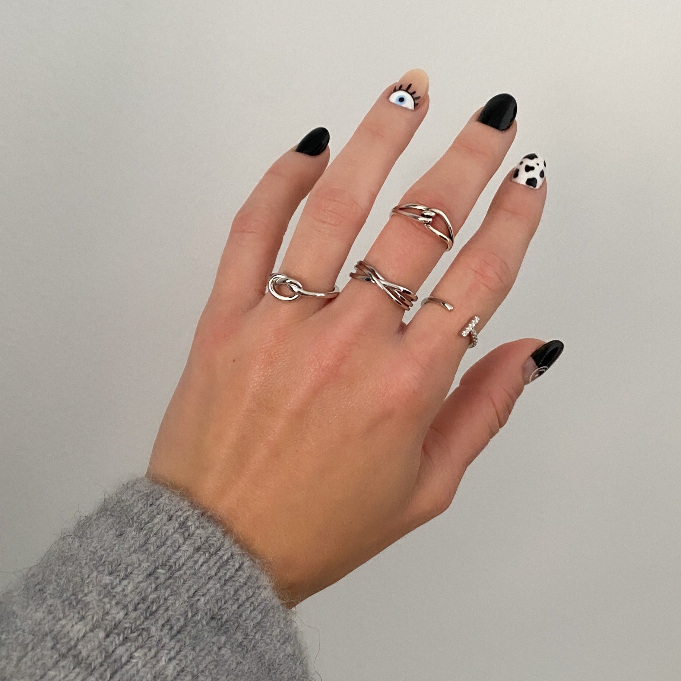 A simple silver ring with a unique design, featuring a knot-like pattern worn by a person on a hand.