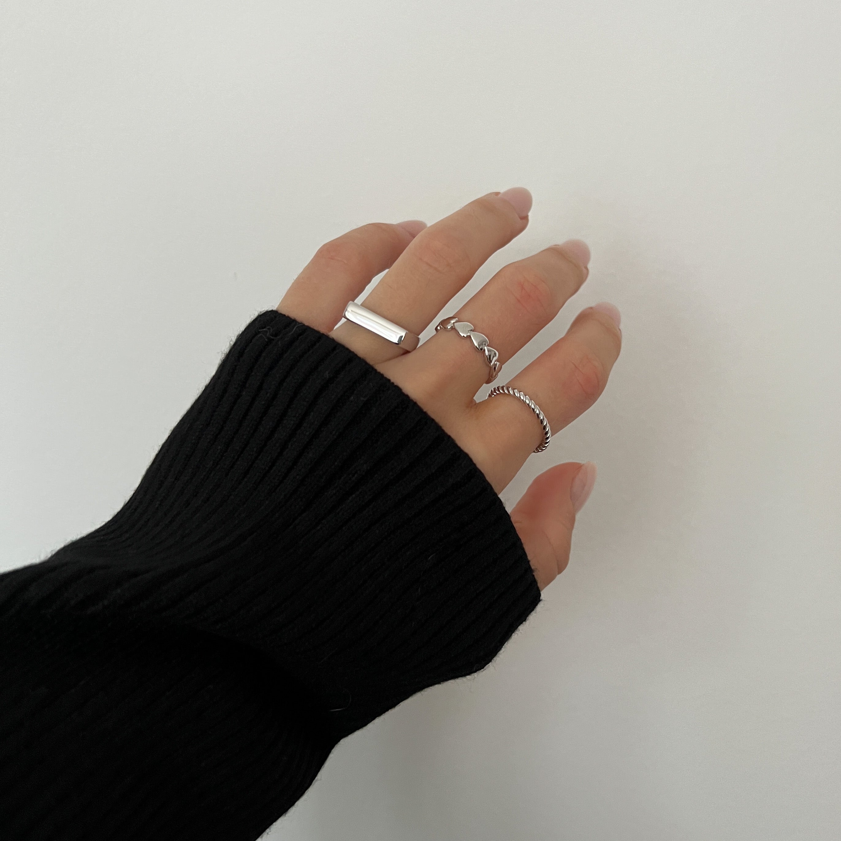 A silver ring with a twisted band design worn by a hand with a black sweater.